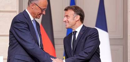 Friedrich Merz zieht das Sakko an, dann fällt Emmanuel Macron ihm um den Hals